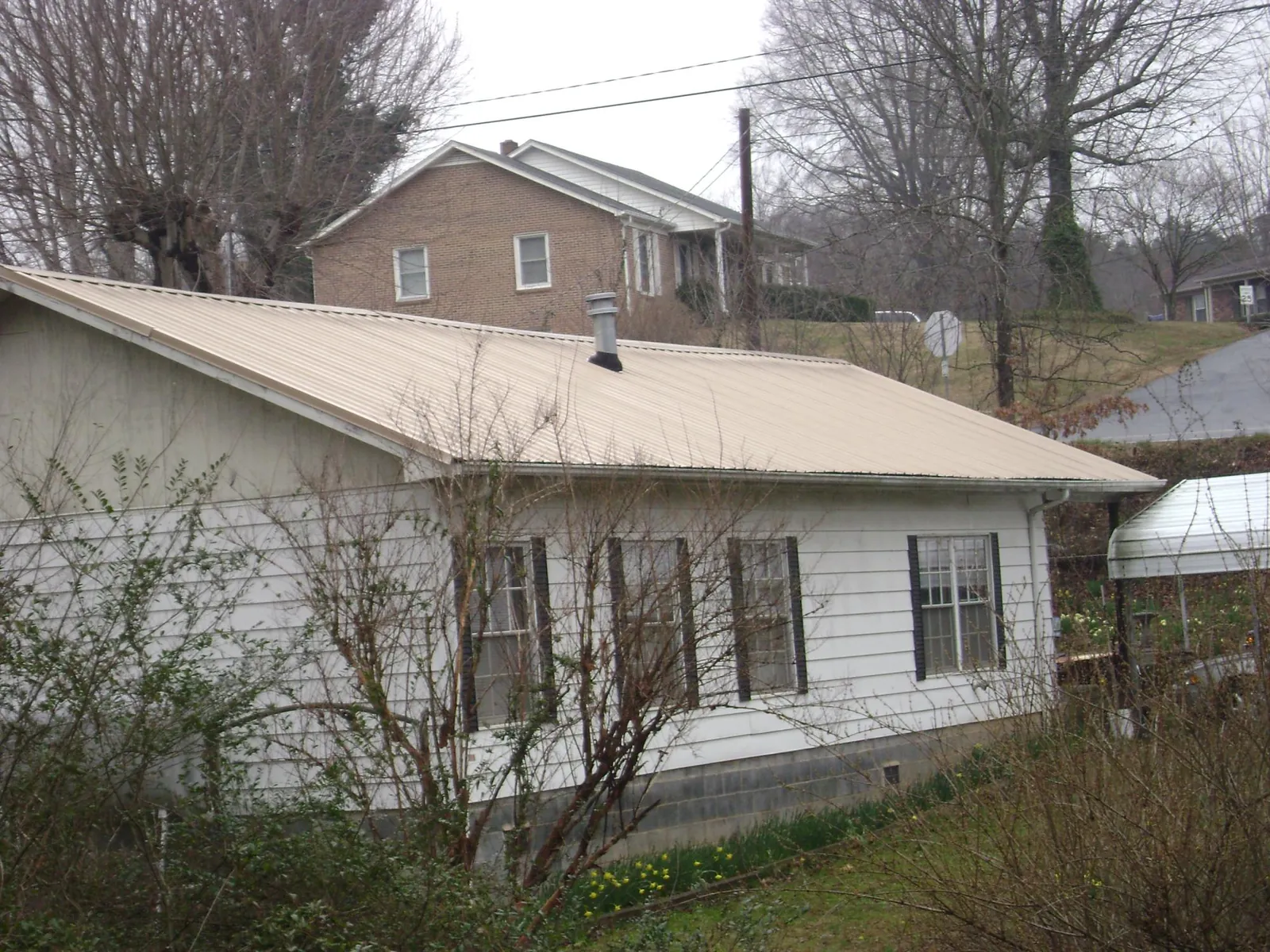Tan metal roof on a white sided house set into a hillside — Commercial Roofing by Roofing Brothers in Strasburg